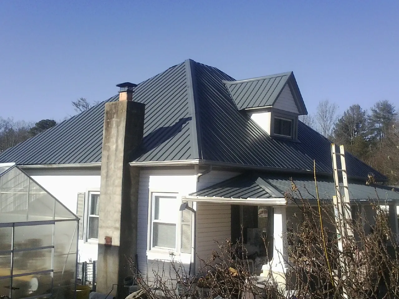 Dark blue standing seam metal roof on a white farmhouse with dormer — Slate & Tile Roof Repair by Roofing Brothers in Moriches