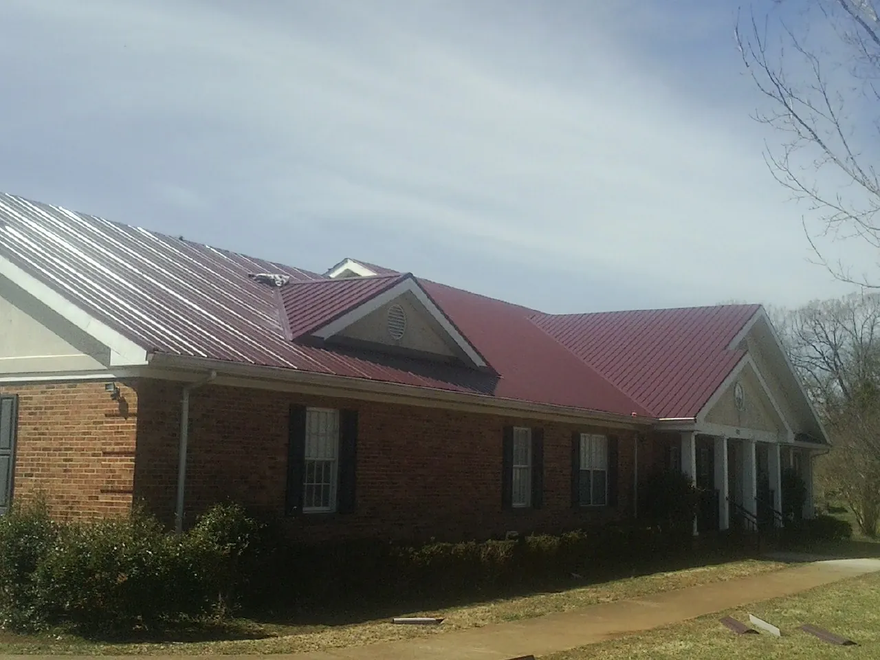 Red metal roof with gabled entries on a long brick building, from a Hail Damage Roof Repair job in Moriches