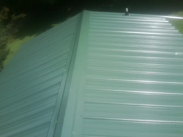 New green metal panels meeting at the ridge of a roof — Flat Roof Repair work by our crew in Moriches