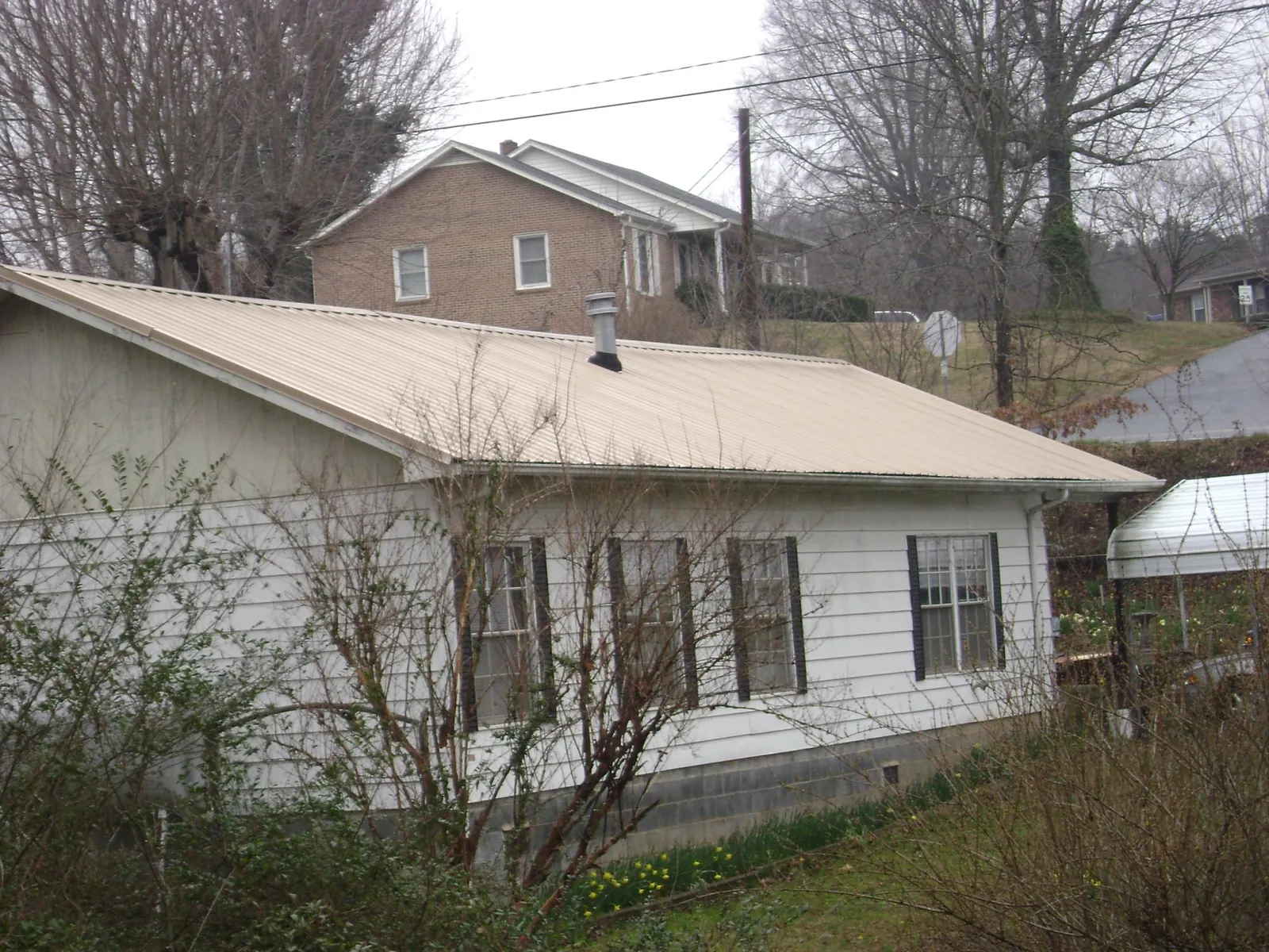 Tan metal roof on a white sided house set into a hillside — Commercial Roofing by Roofing Brothers in Moriches