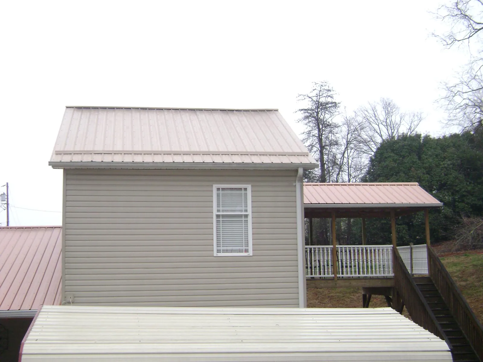 Tan metal roofs on a two story addition and attached porch, from a Roof Replacement job in Moriches